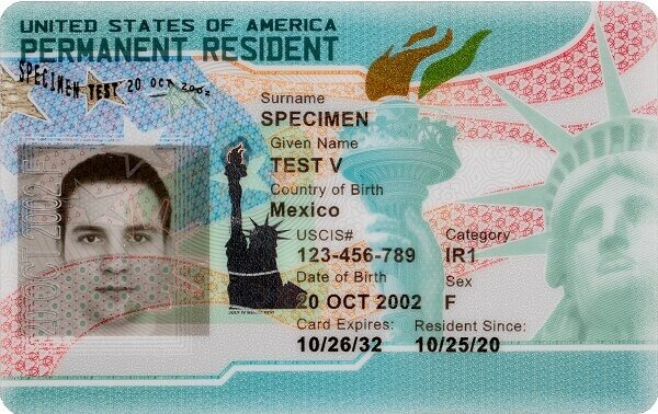 USCIS 官方 SPECIMEN 绿卡正面:顶部为 UNITED STATES OF AMERICA 与 PERMANENT RESIDENT 字样,左侧为示范人像,右侧依次为姓氏 SPECIMEN、名字 TEST V、出生国、USCIS# 示例号码、类别 IR1、出生日期、卡片到期日与成为居民日期,背景为自由女神像与火炬图案。